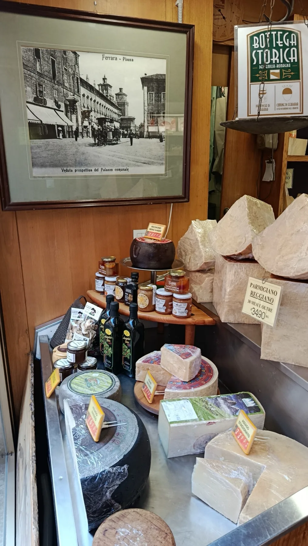 Interno della Bottega del Formaggio: stampa storica della Piazza di Ferrara, parmigiano stagionato e vasetti di confettura